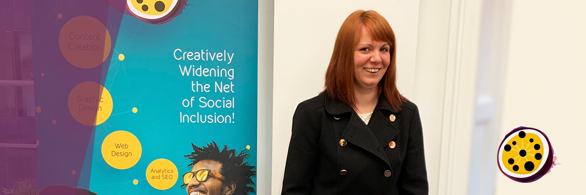 There is a girl in dark coat and ginger hair in the room. She is smiling. Behind her there is a poster with green background and white text that reads Creatively widening the net of social inclusion