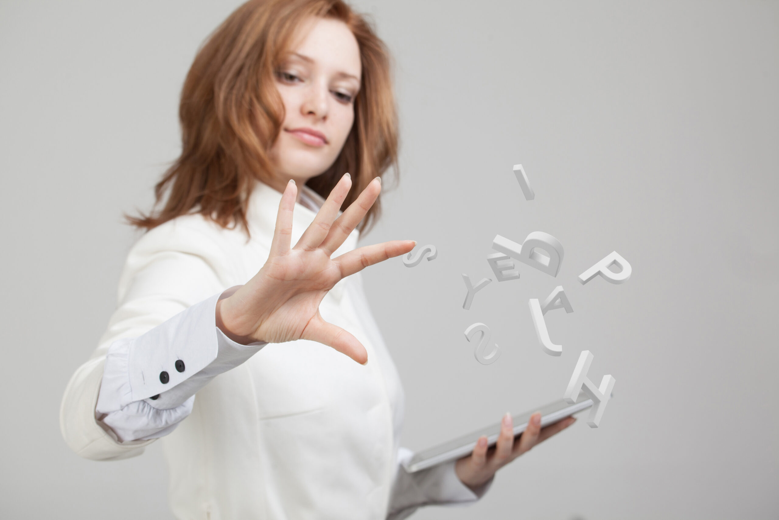 Woman with ginger hair is holding a notepad. She is wearing a white shirt. She is working with the set of letters int he air to wrote concept.