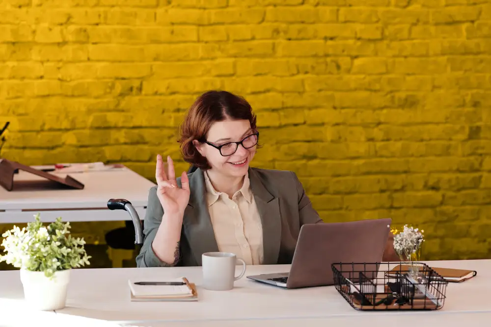 a woman working on her laptop at a white desk in front of a yellow brick wall