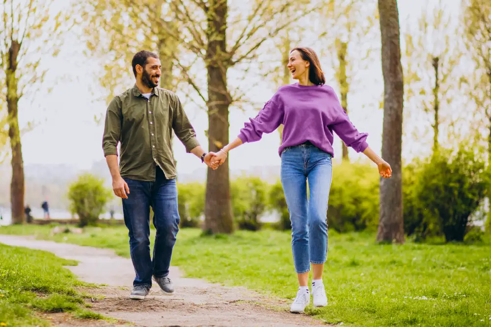 a man and a woman walking while holding hands in a park