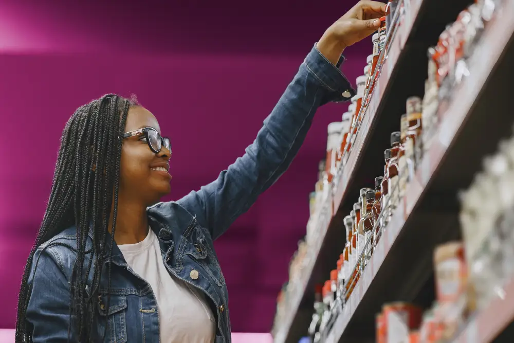 a woman picking something from the top shelf in a supermarket aisle with a purple wall in the background
