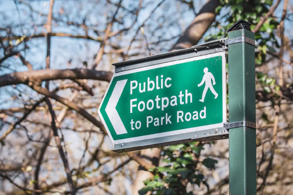 trees in the background and in the foreground a green sign with white text for a public footpath