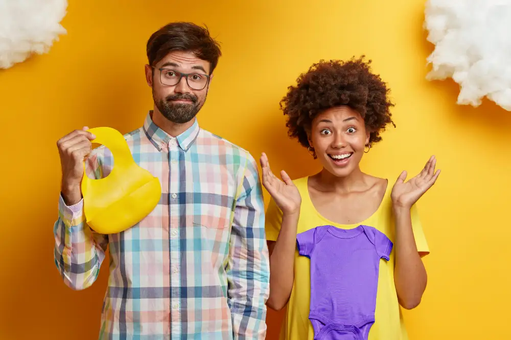 man and a woman holding baby clothes standing in front of a bright yellow wall