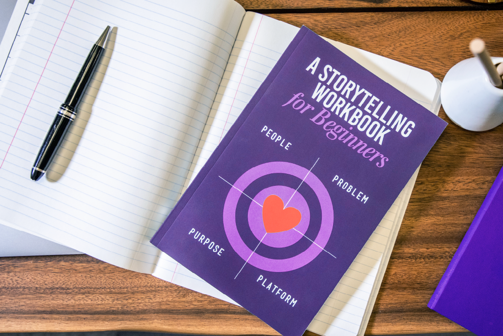 a purple book with the title A Storytelling Workbook for Beginners with a purple target and a loveheart in the centre and in the words People, Problem, Platform and Purpose around the target in a clockwise direction