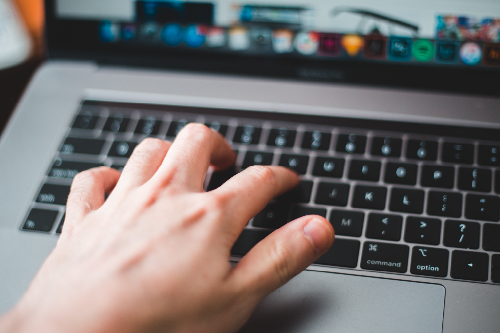 A black laptop keyboard with a hand typing. The laptop's screen is blurred