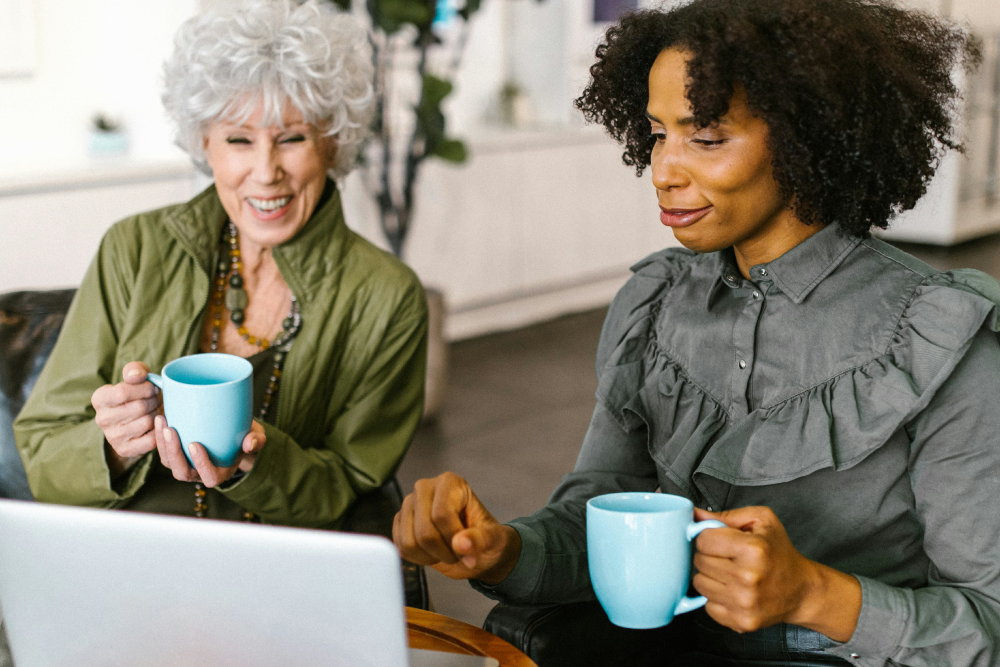 A young woman and an older woman holding a blue mug each looking at a computer screen