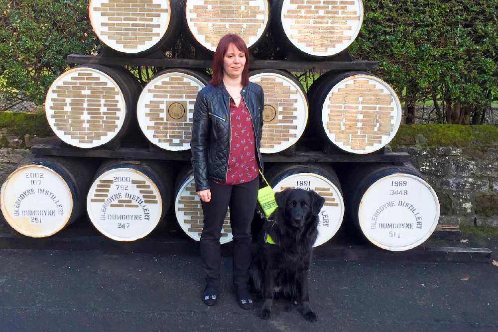 A woman standing with her black Labrador in front of vintage decorative barrels