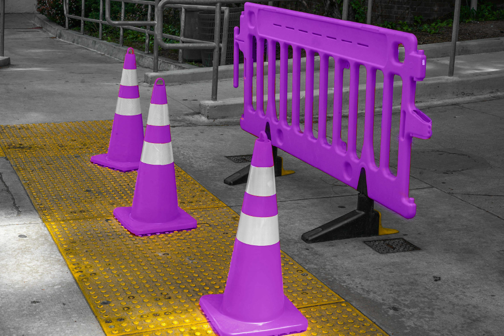 A street with 3 purple cones sitting on a yellow grate next to a purple barrier