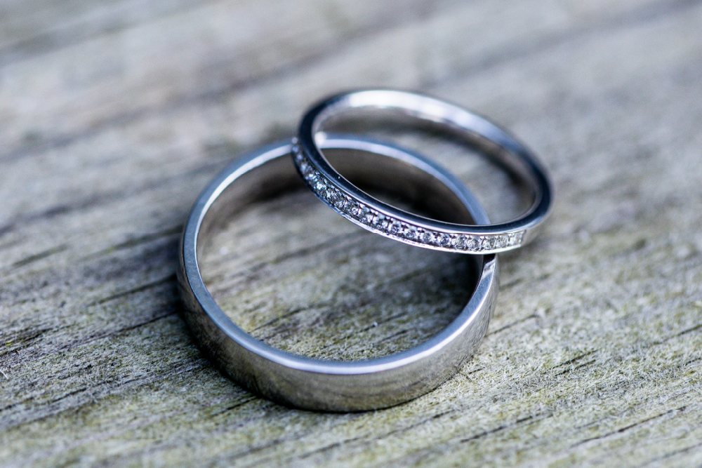 A close-up of two silver wedding rings resting on a textured wooden surface.
