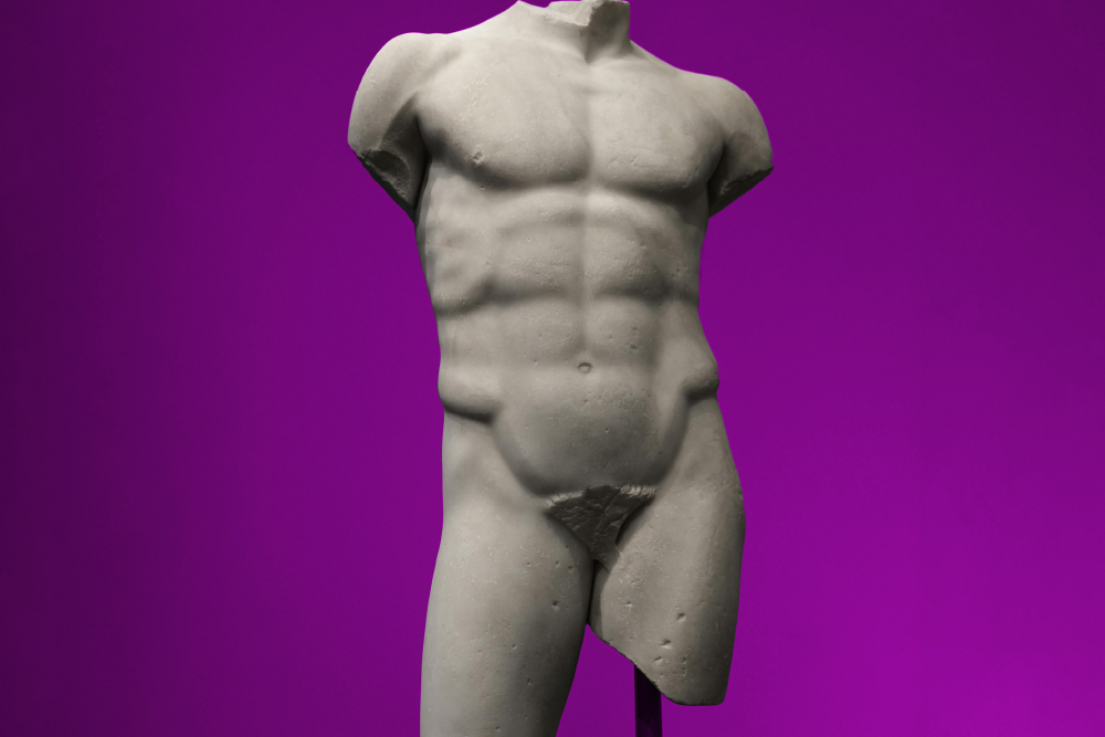 A marble statue torso and thighs of a muscular male figure against a solid purple background, showcasing classical Greek-style sculptural