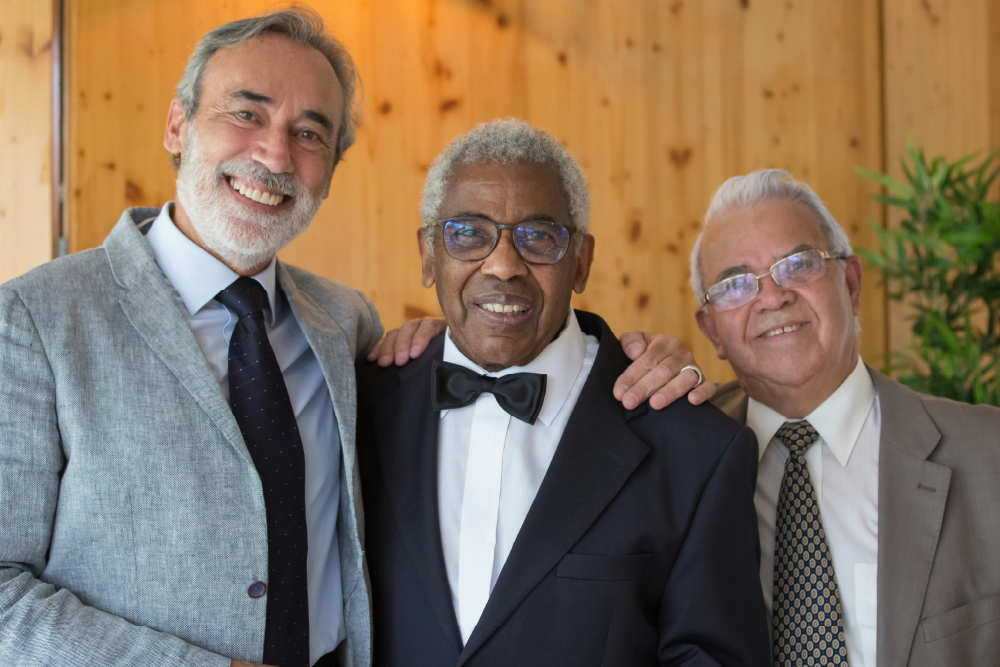 Three elderly men dressed in formal wear, smiling warmly and standing close together