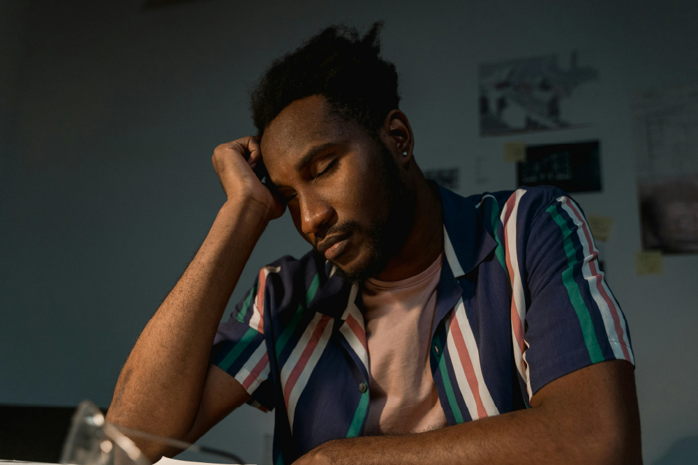 A young man looking tired, resting his head on his hand while seated at a desk
