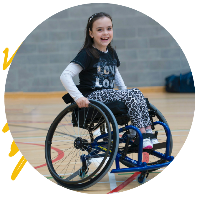 A young girl in a wheelchair smiling. She has long dark hair and leggings with leopard print