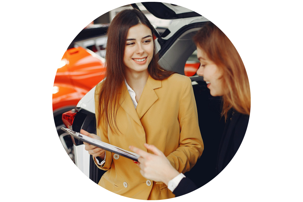 Two women having a conversation in front of a car, one is holding a clipboard