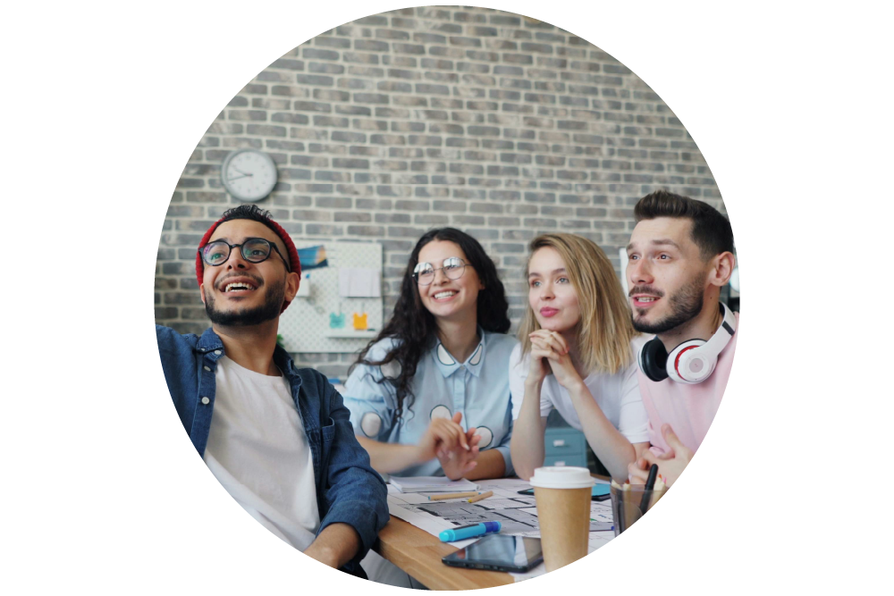 A diverse group of young people at a desk engaged in discussion, there is a brick wall background