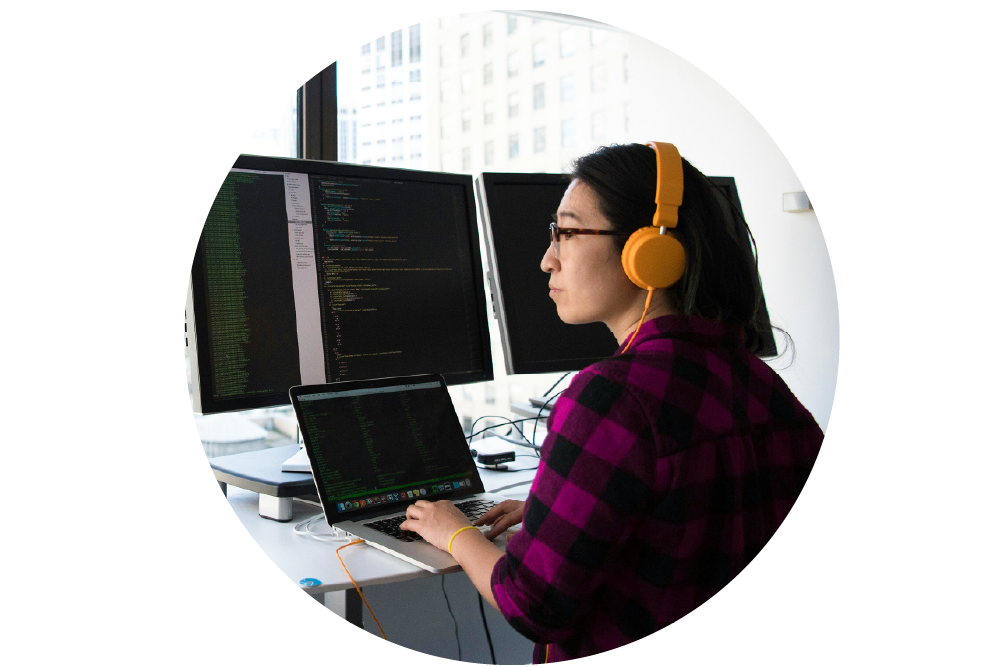 A software developer at work, wearing headphones, sitting at a desk with multiple monitors