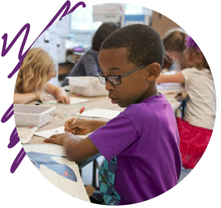 A boy is sitting at a desk painting, wearing a purple T-shirt and glasses. Around him, other children are also painting