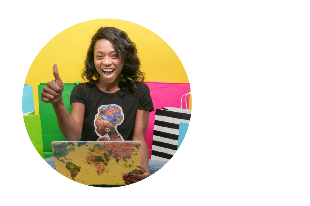 A person with dark curly hair sitting with a laptop that has a world map design on its cover. They're giving a thumbs up and smiling enthusiastically. Behind them are colourful shopping bags in green, pink, and black and white stripes against a bright yellow background.