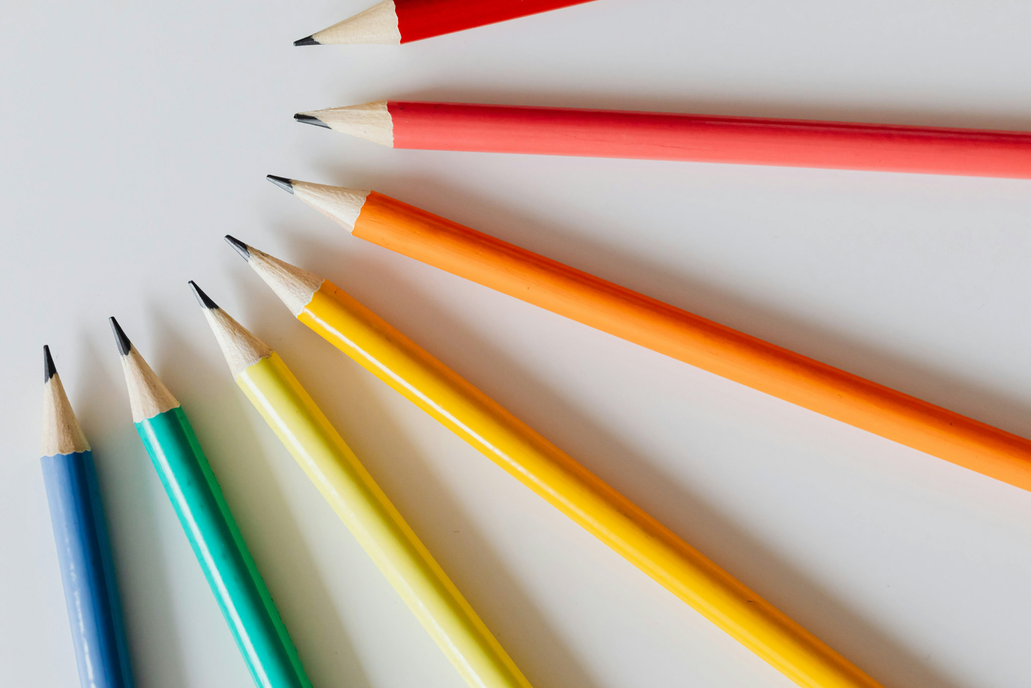 Red, orange, yellow, green, and blue pencils laid out to form a semi-circle in rainbow colours against a white background.