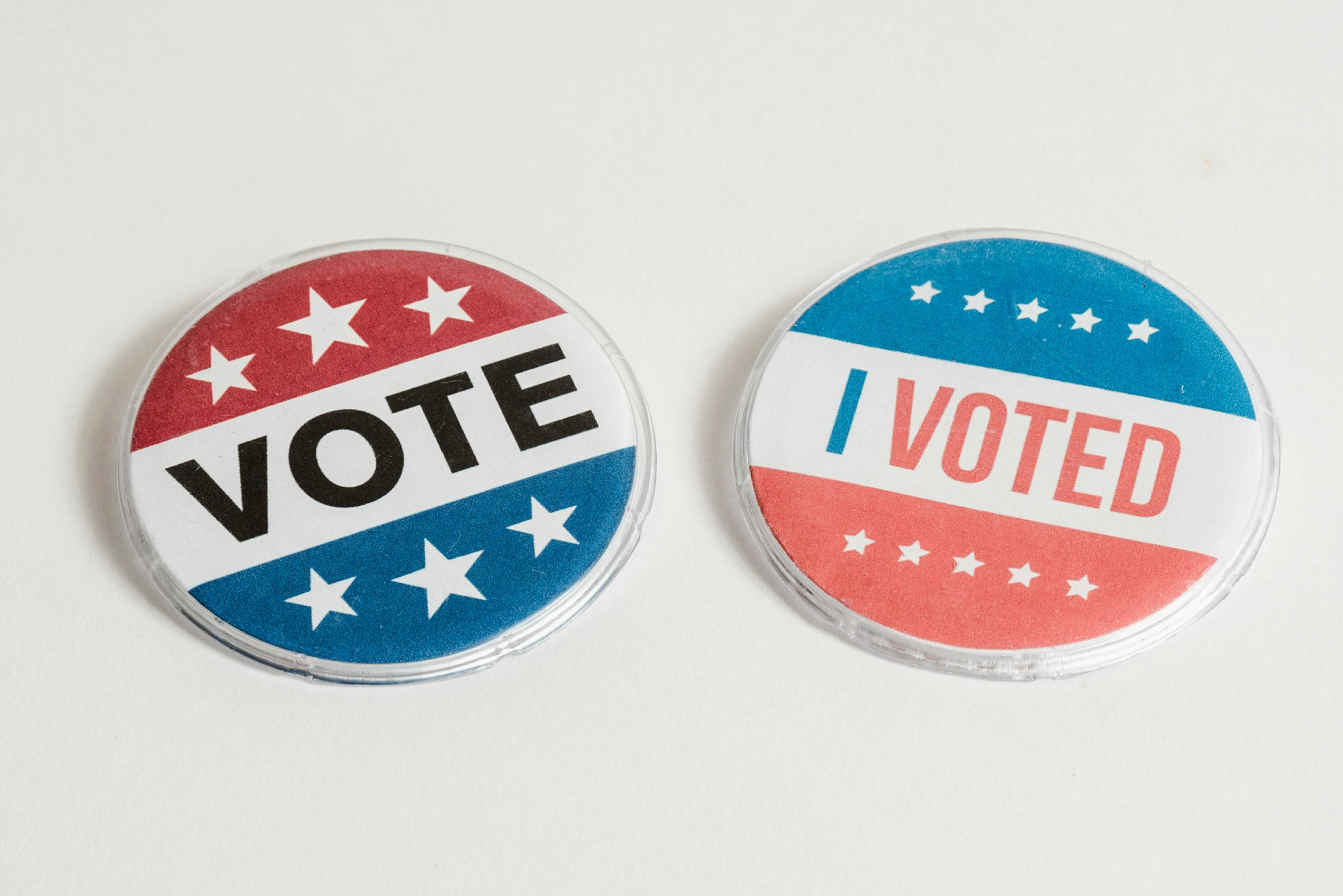 A white background with two red, white and blue pin badges with star graphics and the text ‘Vote’ and ‘I voted’.