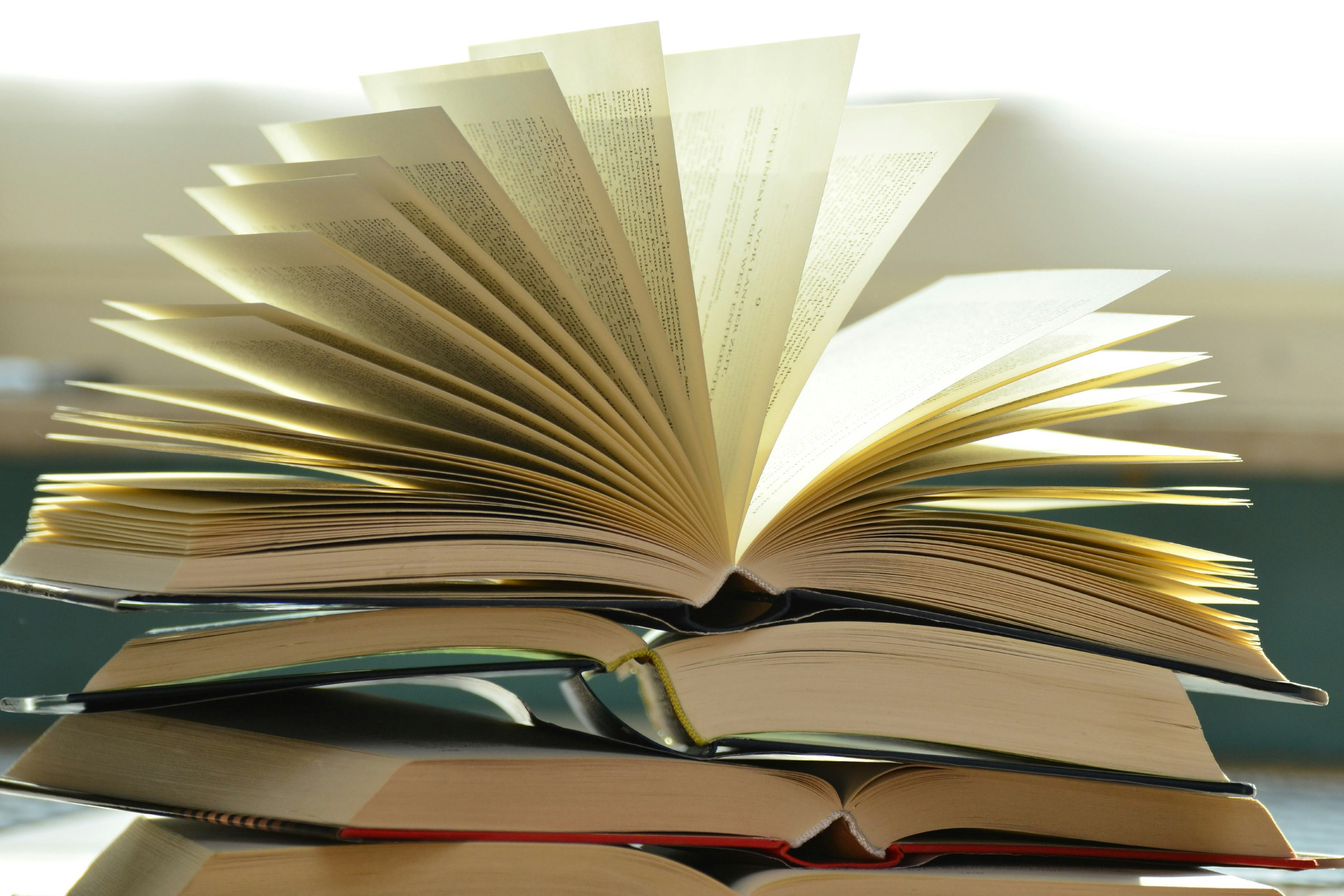 A stack of four open books. The pages on the book topping the stack are spread open.