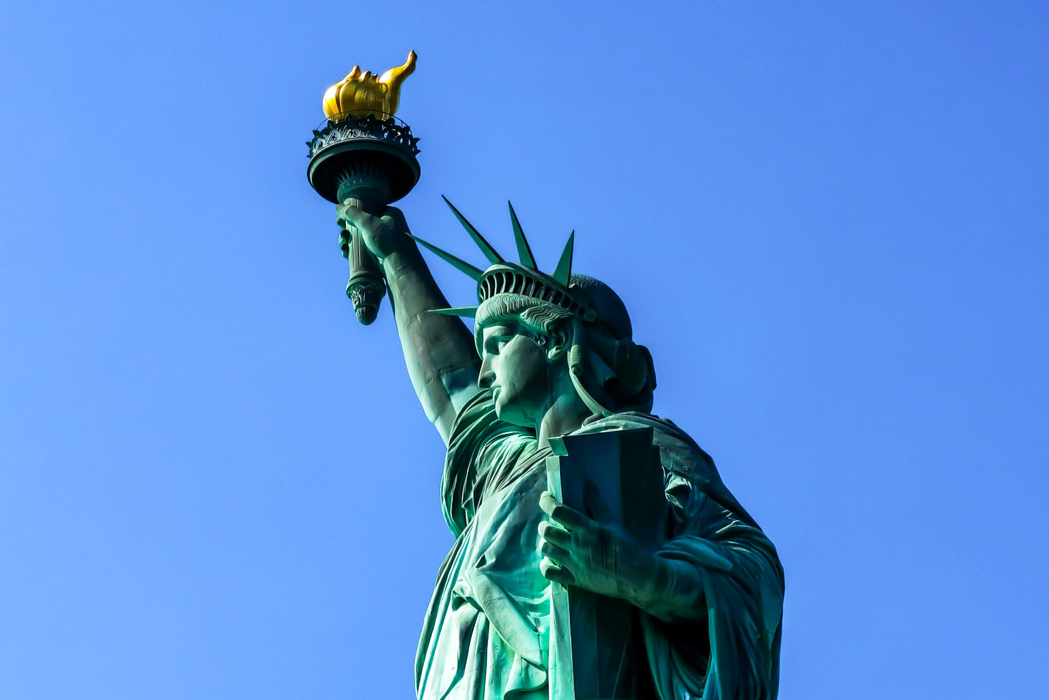 A profile of the head and torso of the Statue of Liberty against a blue sky.
