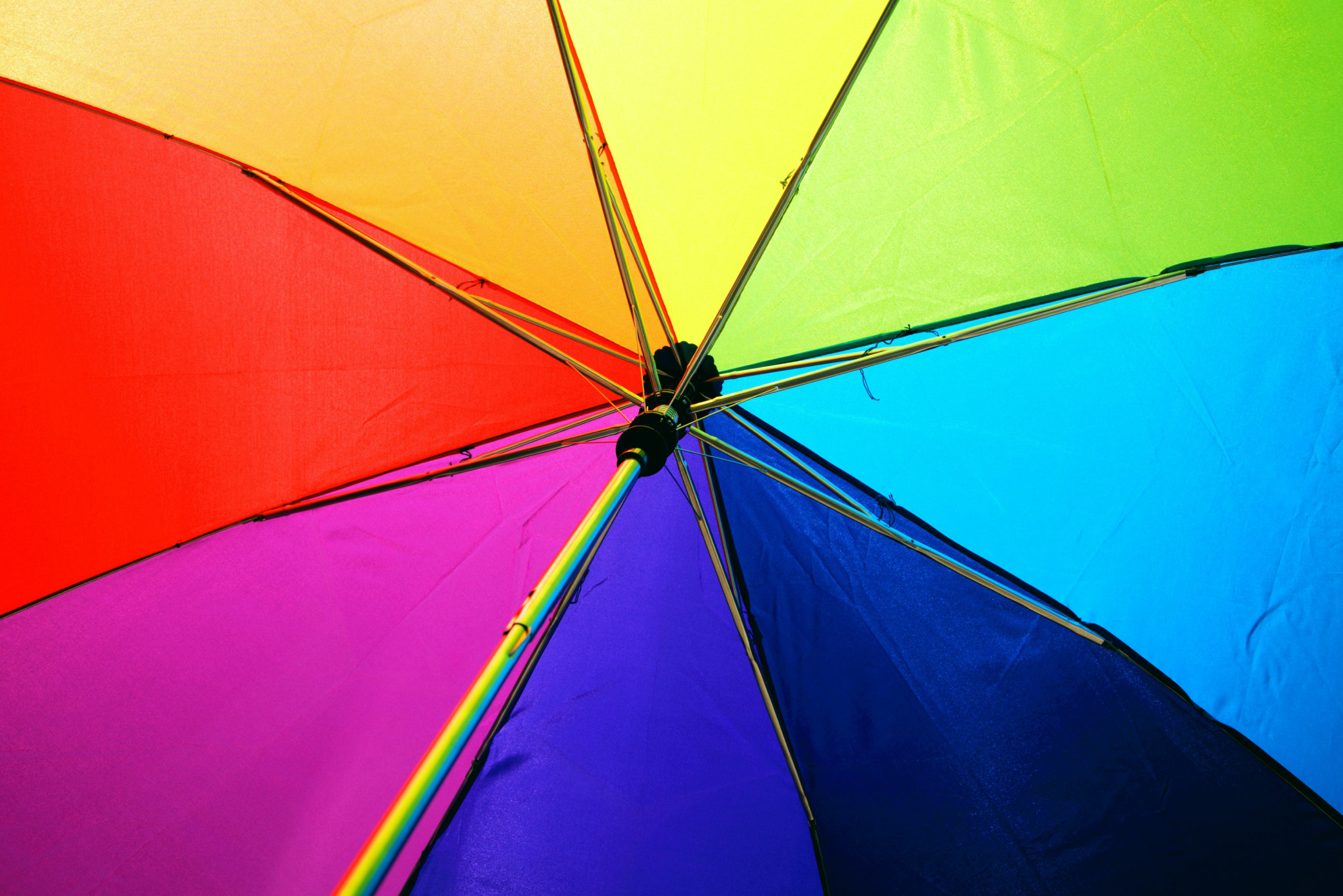 The underside of a rainbow coloured umbrella with red, orange, yellow, green, blue and purple segments.