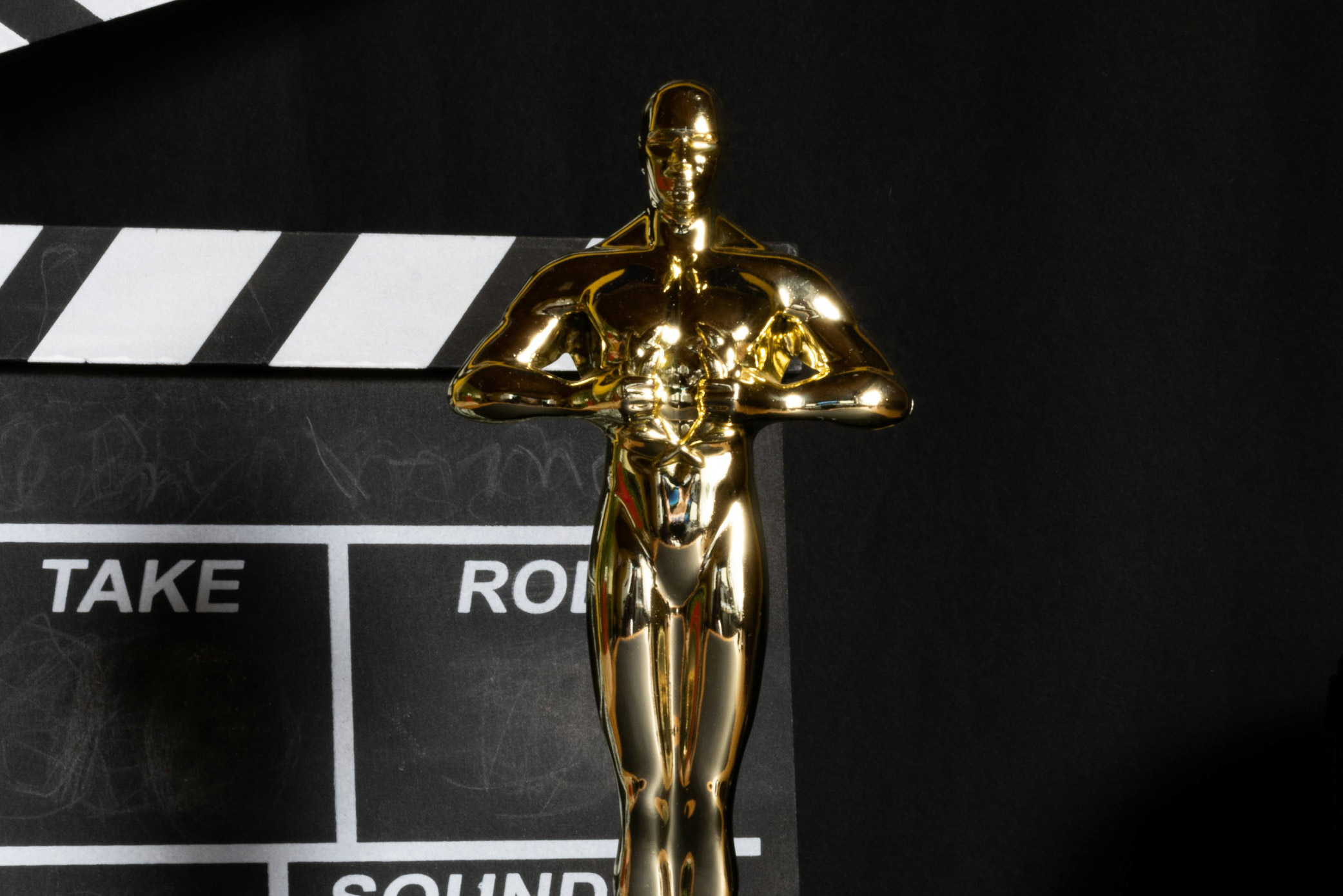 A gold Academy Awards trophy with a black and white clapperboard against a black background.