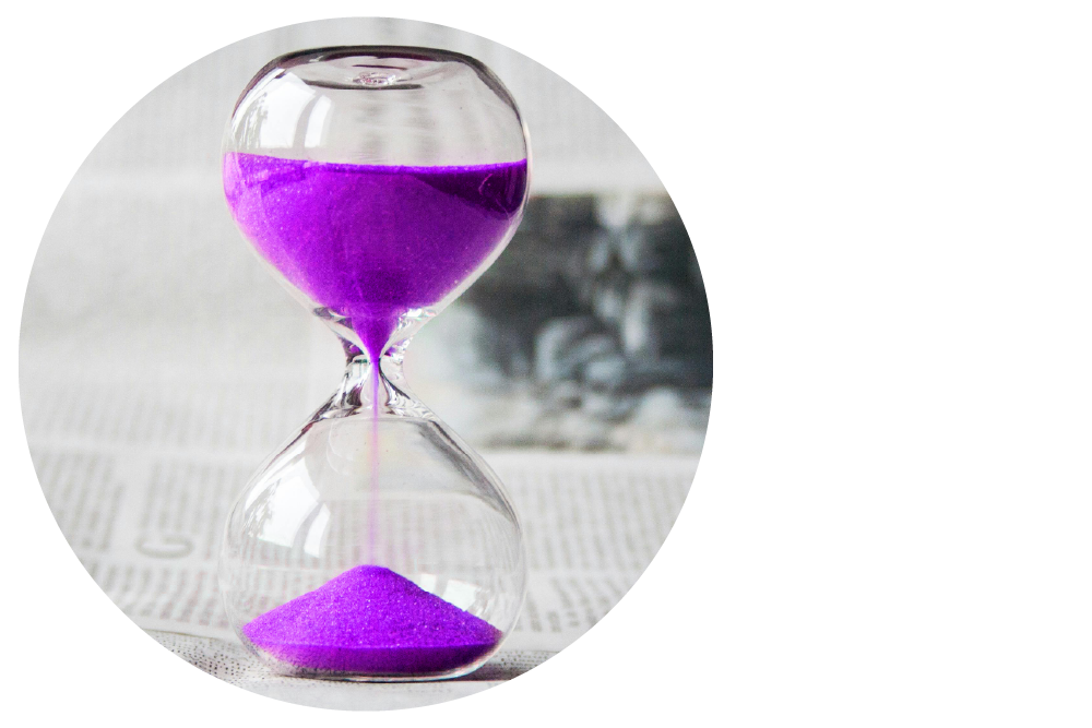 a glass sand timer containing purple sand on top of a newspaper on a table 