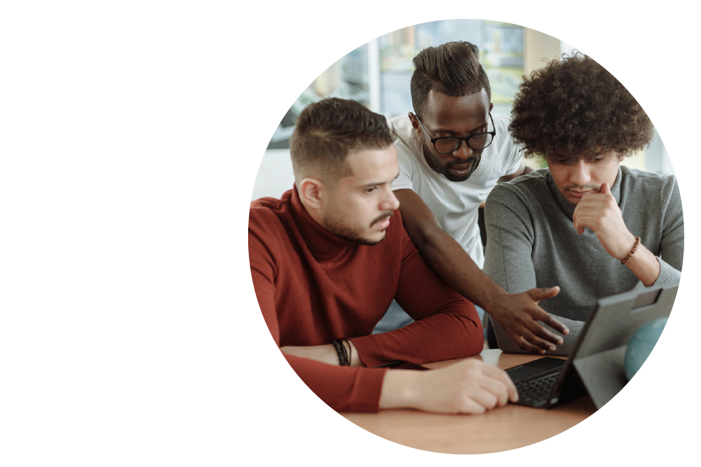 three people at a desk, gathered around a laptop computer with thoughtful expressions.