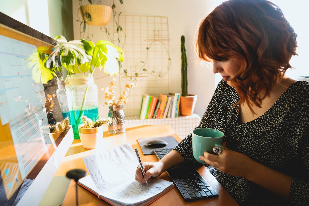 Woman writing notes at a desk while working on a computer