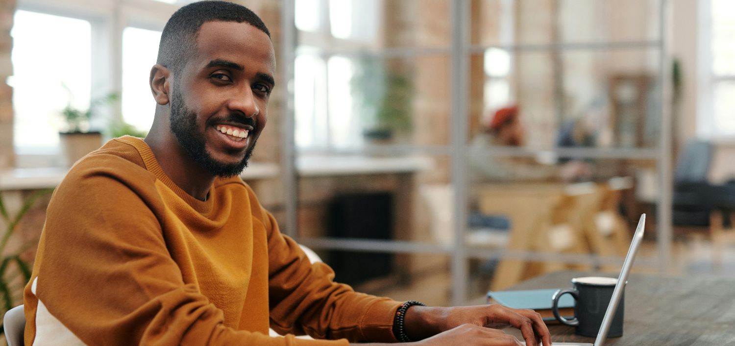 Man smiling while working on a laptop in an open plan office
