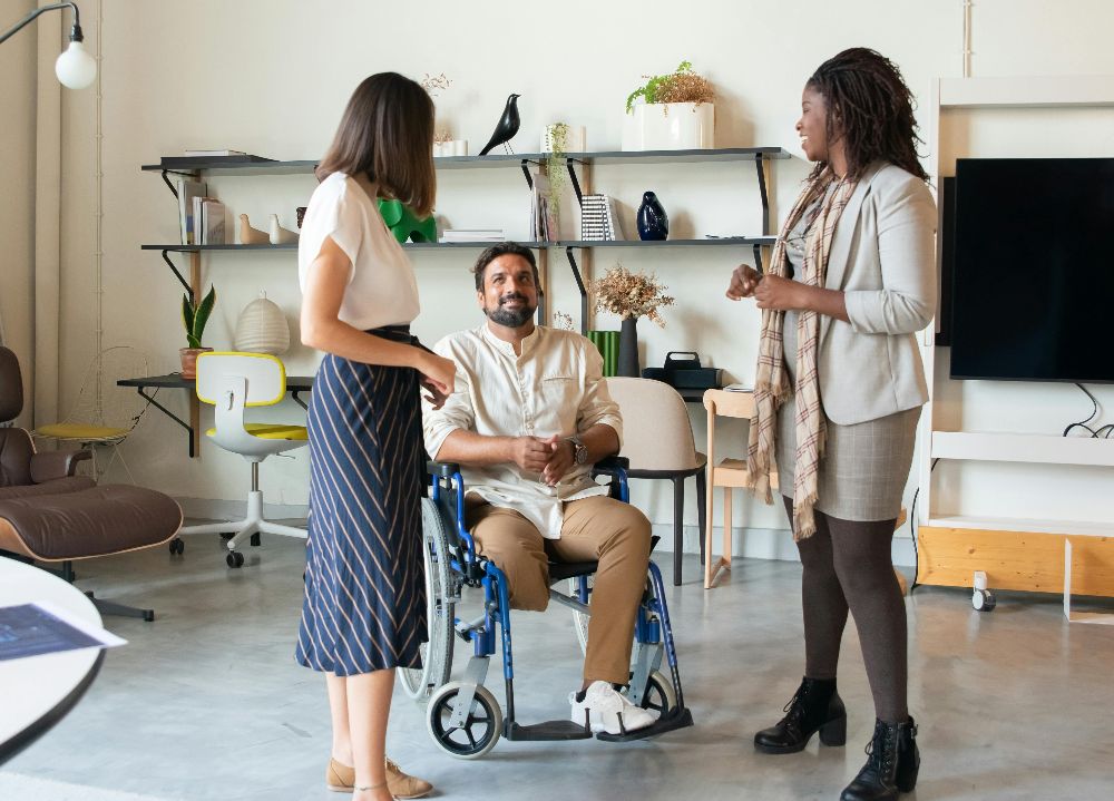 Three colleagues talking in an office, one using a wheelchair