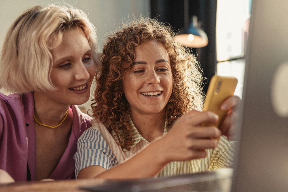 Two women smiling and looking at a phone together