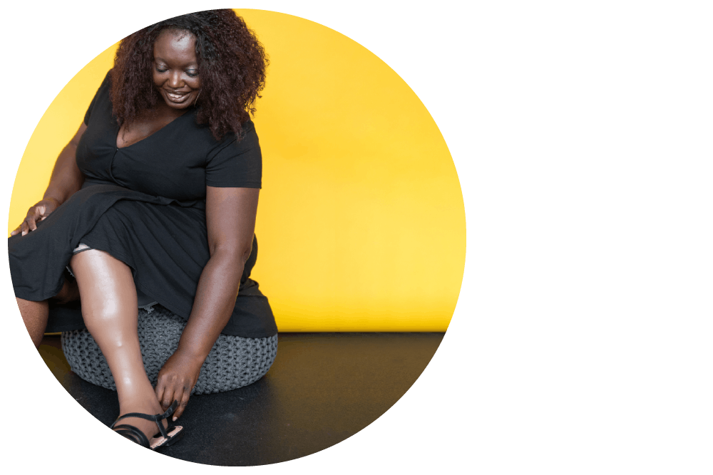 a smiling Black person sitting on a bean bag chair and adjusting their footwear.