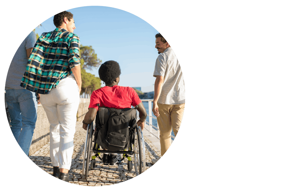 four people, one of whom is a wheelchair user, on a sunny waterfront walkway.