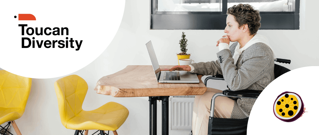 Person in wheelchair working on laptop at wooden desk with Toucan Diversity logo in corner