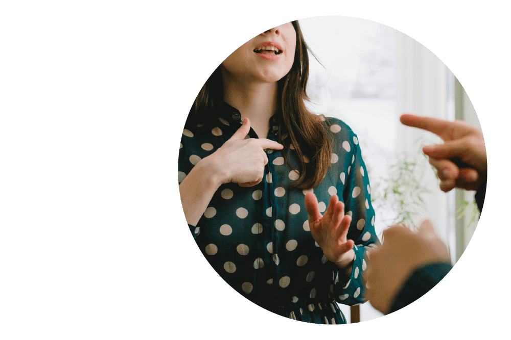 two people conversing using sign language. The first person is facing the second their torso, and their hands are visible within the frame. The second person is facing away from the camera and only their hands are visible.