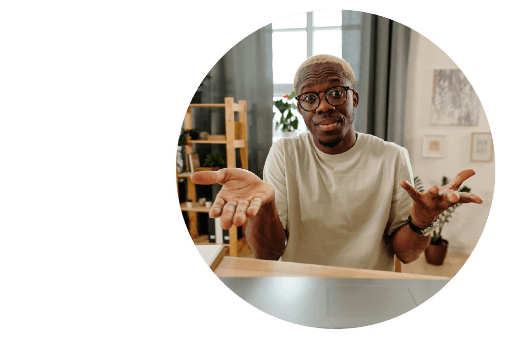 a person sitting at a desk, shrugging their shoulders with open palms and a confused expression.