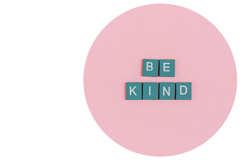 6 blue tiles with white uppercase letters arranged to spell out ‘be kind’ against a pink background