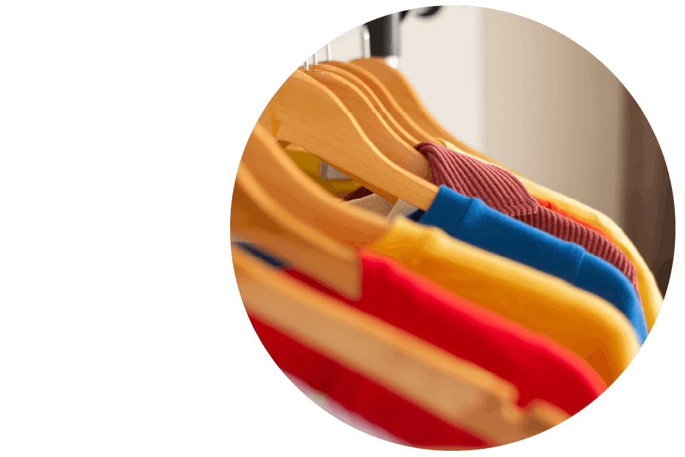 A close-up shot of the collars and shoulders of colourful garments hanging neatly in a row on wooden hangers