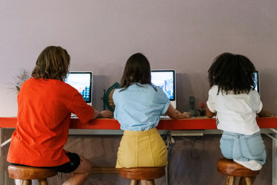 Three people, viewed from behind, sitting on stools and using laptop computers