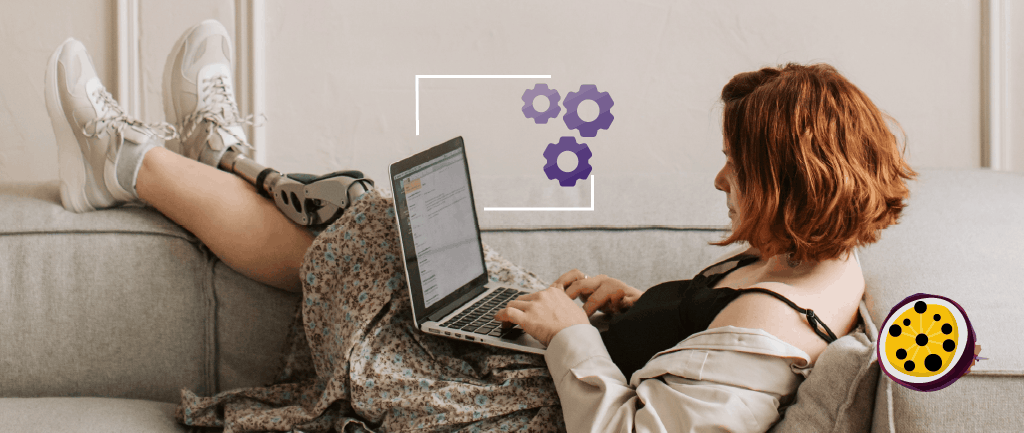 A person with a prosthetic leg reclining on a sofa while working on a laptop. Above the laptop, a graphic shows three purple gears enclosed in a white frame, suggesting they are performing an accessibility audit