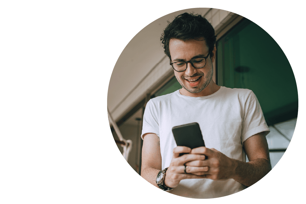 A smiling person looking down at their smartphone while holding it with both hands.